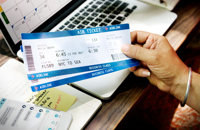 Mano sosteniendo un boleto de avión cerca de una computadora portátil y un calendario, simbolizando la aprobación de estadía familiar sin el consentimiento de la esposa.