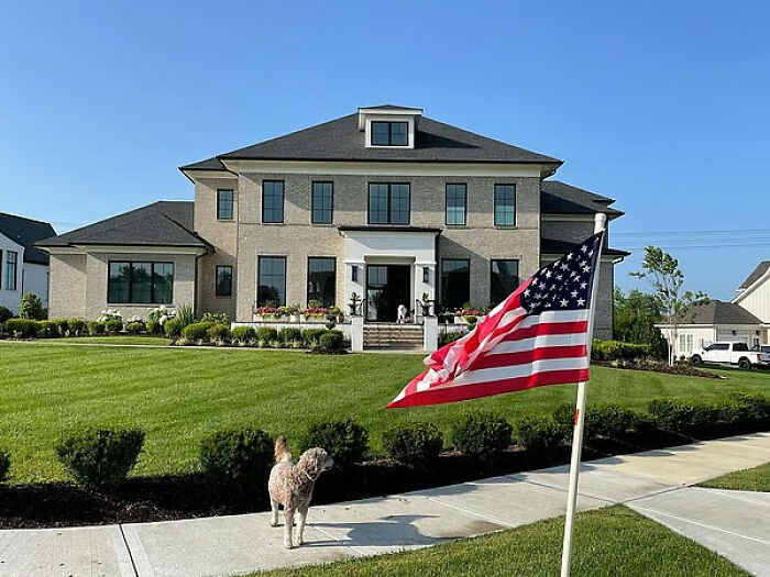 Casa grande y moderna con césped cuidadosamente recortado y bandera estadounidense en el patio delantero como vecino en pelea con la estrella de Reacher, Alan Ritchson.