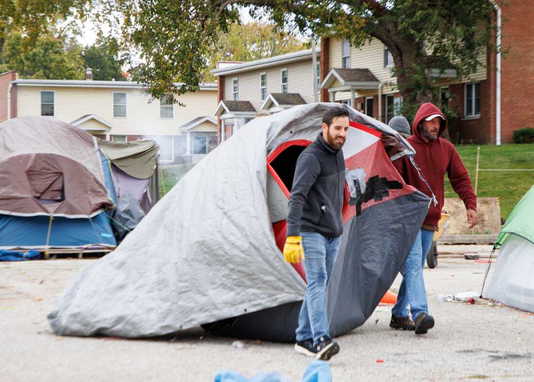 Un empleado de Home Sweet Home Ministries y un voluntario arrastran una tienda de campaña hasta un contenedor de basura en el estacionamiento de una iglesia que se estaba utilizando como campamento para personas sin hogar.