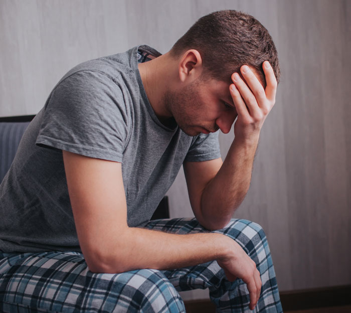 Hombre vestido con ropa informal sentado con la cabeza en la mano, mostrando dolor y dolor emocional después del cruel comentario de su esposa embarazada.