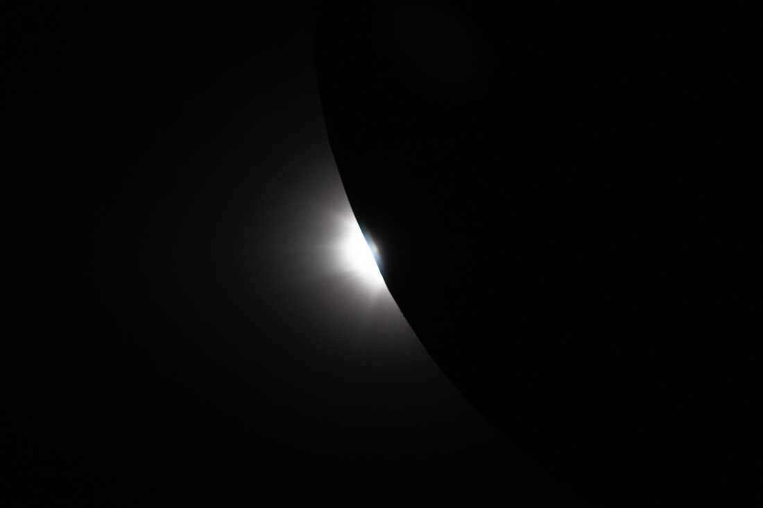 art002e009299 (April 6, 2026) – Captured from the Orion spacecraft near the end of the Artemis II lunar flyby on April 6, this image shows the Sun beginning to peek out from behind the Moon as the eclipse transitions out of totality. Only a portion of the Moon is visible in frame, its curved edge revealing a bright sliver of sunlight returning after nearly an hour of darkness. In final moments of the eclipse observed by the crew, the reemerging light creates a sharp contrast against the Moon’s silhouette and reveals lunar topography not usually visible along the lunar limb. This fleeting phase captures the dynamic alignment of the Sun, Moon, and spacecraft as Orion continues its journey back from the far side of the Moon.