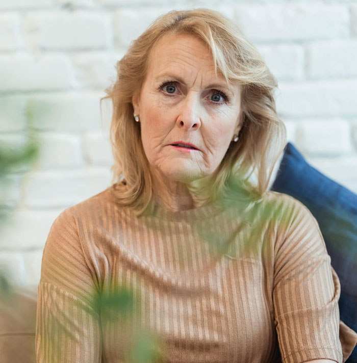 Mujer mayor con expresión preocupada sentada en el interior, reflejando el dilema sobre la madre que controla el arreglo para dormir con la futura esposa